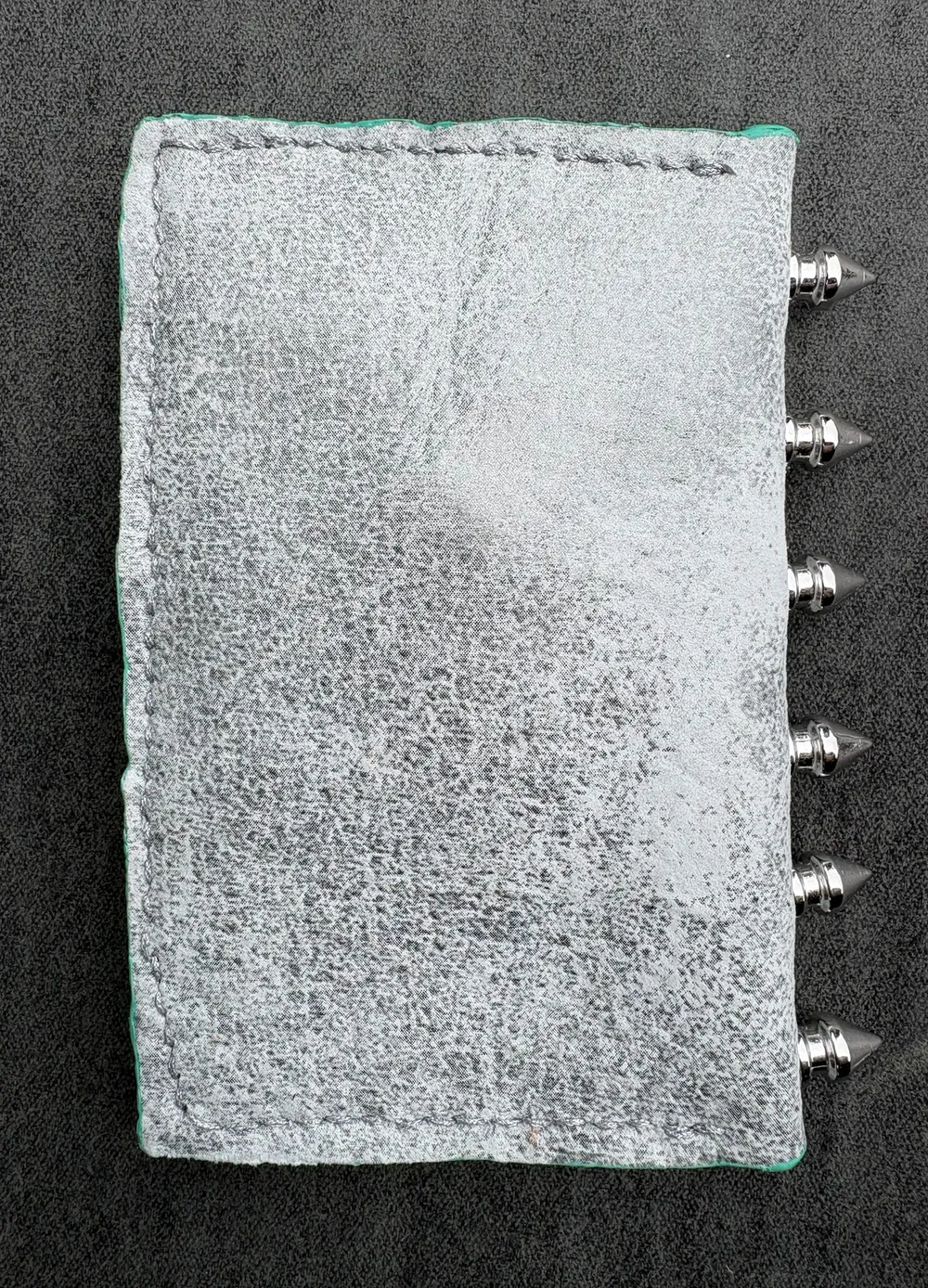 Back of wallet showing white and silver leather, silver stitching along three sides, and silver spikes on spine