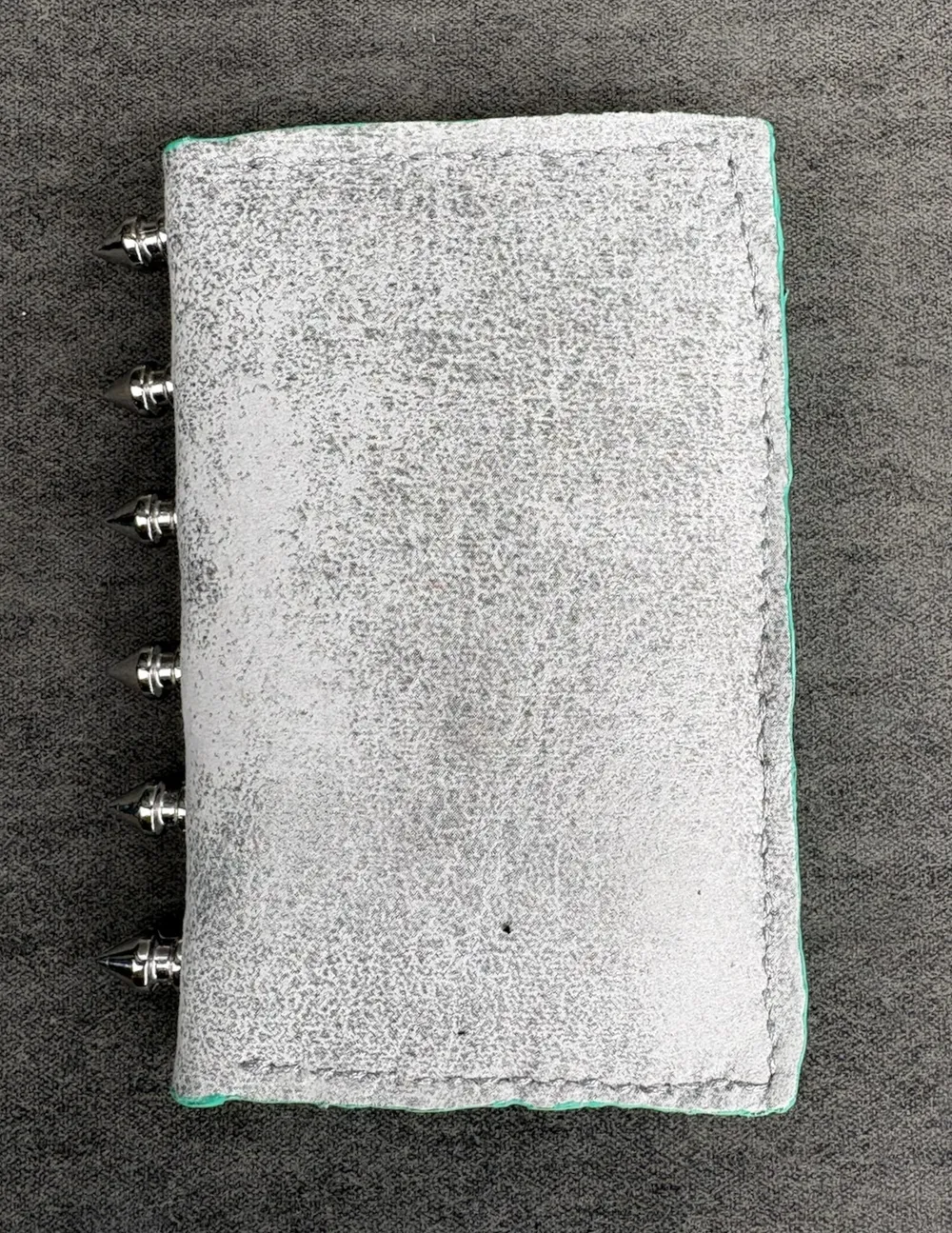 Front of wallet showing white and silver leather, silver stitching along three sides, and silver spikes on spine