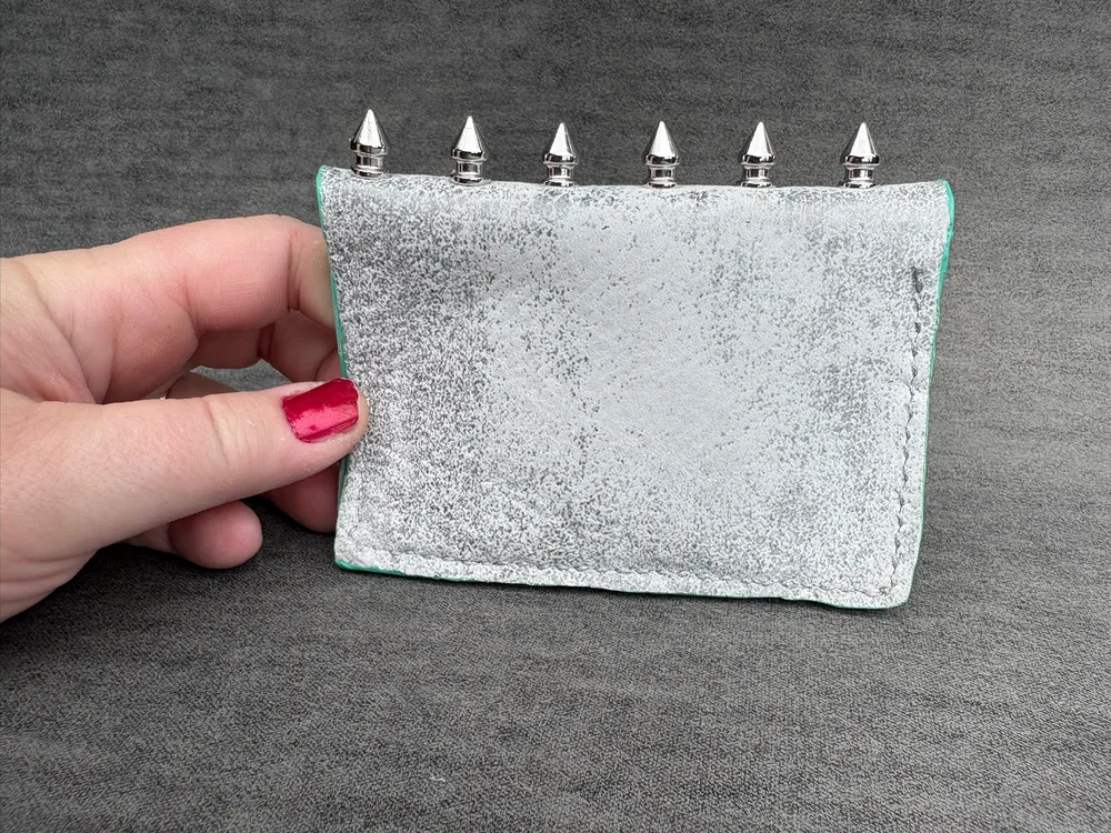 Wallet held by a hand so the spine is at the top and spikes are pointing up